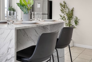 Cozinha moderna com bancadas de mármore, cadeiras pretas e um vaso com planta.