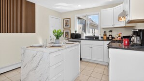 A modern kitchen with white cabinetry, a marble island, and a view of the outside. - Hidden Pines Retreat - Charming 3 bedroom home near Downtown Boston! (Somerville)