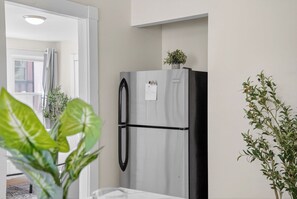 A kitchen with a refrigerator, a window with curtains, and potted plants.