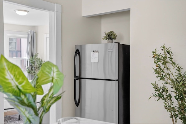 Una cocina con un refrigerador, una ventana con cortinas y plantas en macetas.
