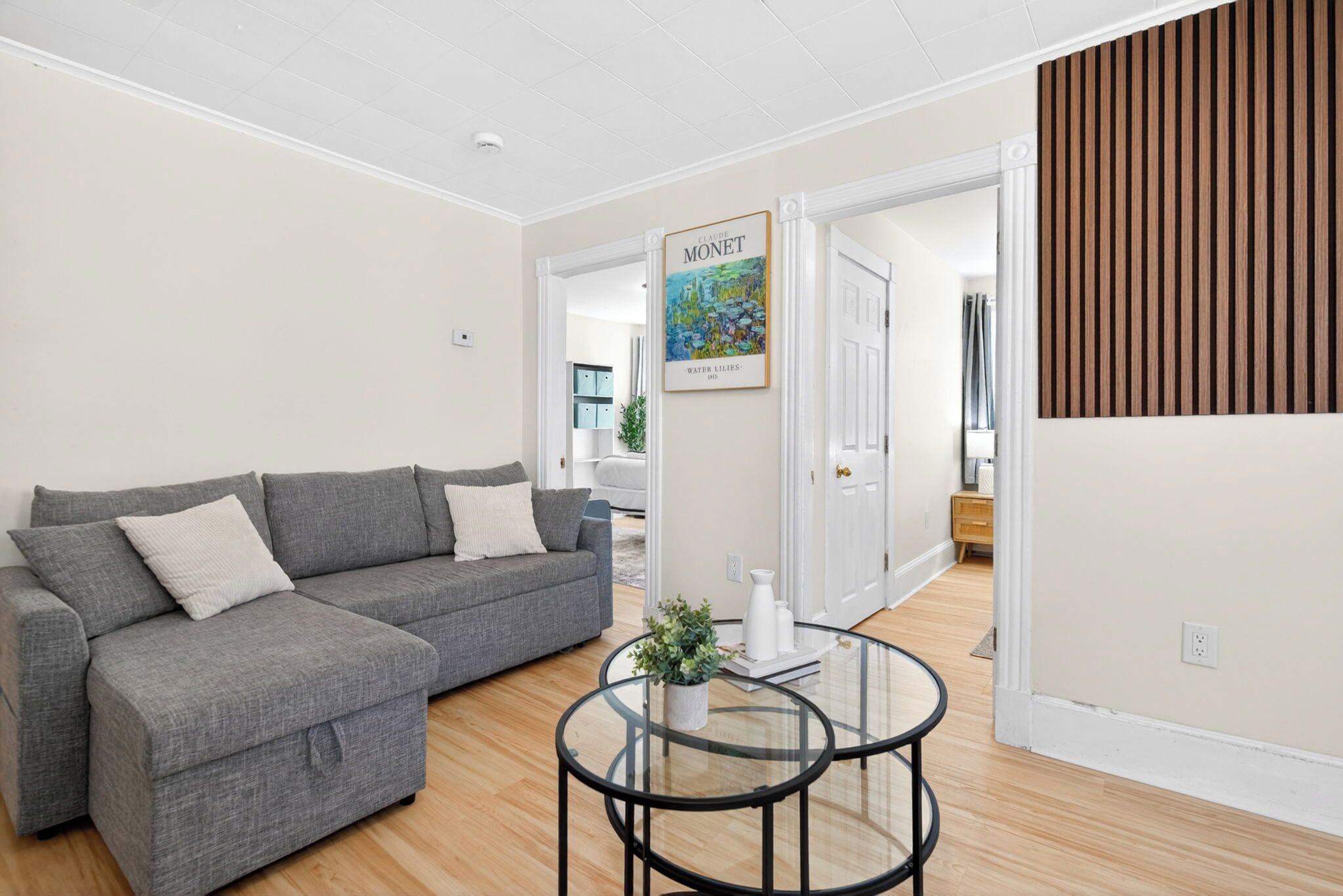 Een moderne woonkamer met een grijze modulaire bank, een glazen salontafel en een ingelijste poster aan de muur.
