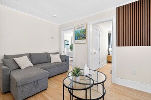 Una sala de estar moderna con un sofá modular gris, una mesa de centro de vidrio y un cartel enmarcado en la pared.