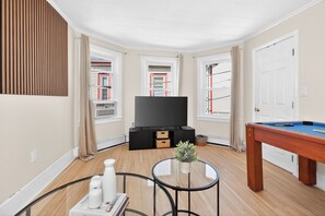 Ein Zimmer mit Flachbildfernseher, Poolbillardtisch, Glastisch und einer Topfpflanze.