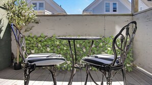 A patio with two metal chairs and a small table, surrounded by a white wall and greenery. - Hidden Pines Retreat - Charming 3 bedroom home near Downtown Boston! (Somerville)