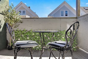 Um pátio com duas cadeiras de metal e uma mesa pequena, cercado por um muro branco e vegetação.