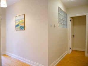 Een hal met een schilderij aan de muur, een raam met geëtste glas, en een deur die naar een andere kamer leidt.