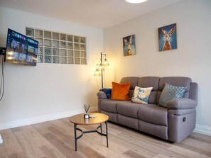 Ein Wohnzimmer mit einer Couch, einem Couchtisch, einem an der Wand montierten Fernseher und zwei Bildern.