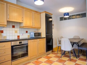 Eine Küche mit Holzausstattung, einer Mikrowelle, einem Kühlschrank, einem Backofen und einem Esstisch mit Stühlen.