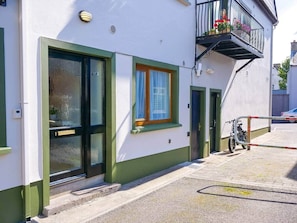 Ein Gebäude mit einer grünen Tür, einem Fenster mit Vorhang und einem Balkon mit Blumen.