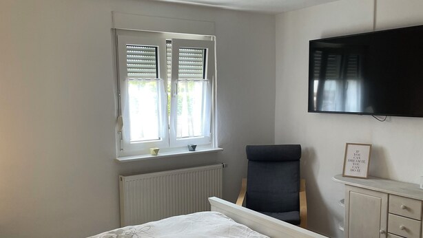 A bedroom with a bed, a chair, a television, and a window with blinds. - Lovingly Renovated Apartment in Hausen (Hausen)