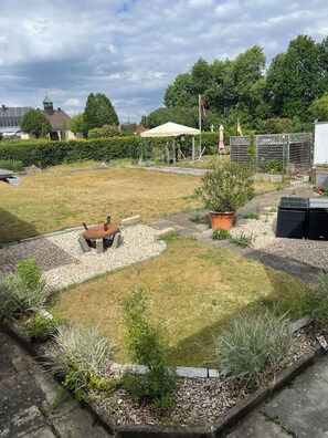 A garden with a wooden bench, a white umbrella, and a small tree.