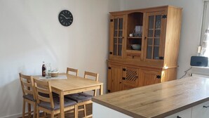 A kitchen with a wooden table and chairs, a cabinet with glass doors, and a clock on the wall. - Lovingly Renovated Apartment in Hausen (Hausen)