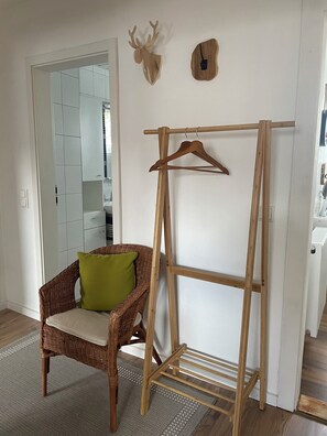 Ein Zimmer mit einem hölzernen Kleiderständer, einem Korbstuhl mit Kissen sowie einem an der Wand befestigten Hirsch-Dekoration.