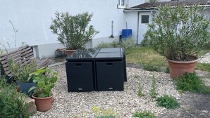A residential garden with a bench, potted plants, and a black outdoor storage unit. - Lovingly Renovated Apartment in Hausen (Hausen)
