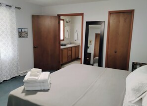 A hotel room with a bed, a bathroom with a sink and mirror, and a door leading to another room. - Charming house in tranquil North Western Mesick, Michigan for a relaxing getaway (Mesick)