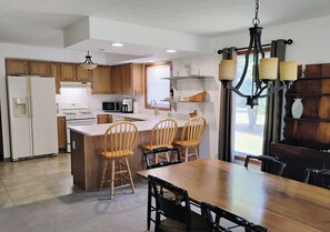 A modern kitchen with wooden cabinets, a central island, and a dining area with a wooden table and chairs. - Charming house in tranquil North Western Mesick, Michigan for a relaxing getaway (Mesick)