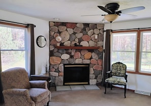 A living room with a stone fireplace, a ceiling fan, a clock, and a chair. - Charming house in tranquil North Western Mesick, Michigan for a relaxing getaway (Mesick)