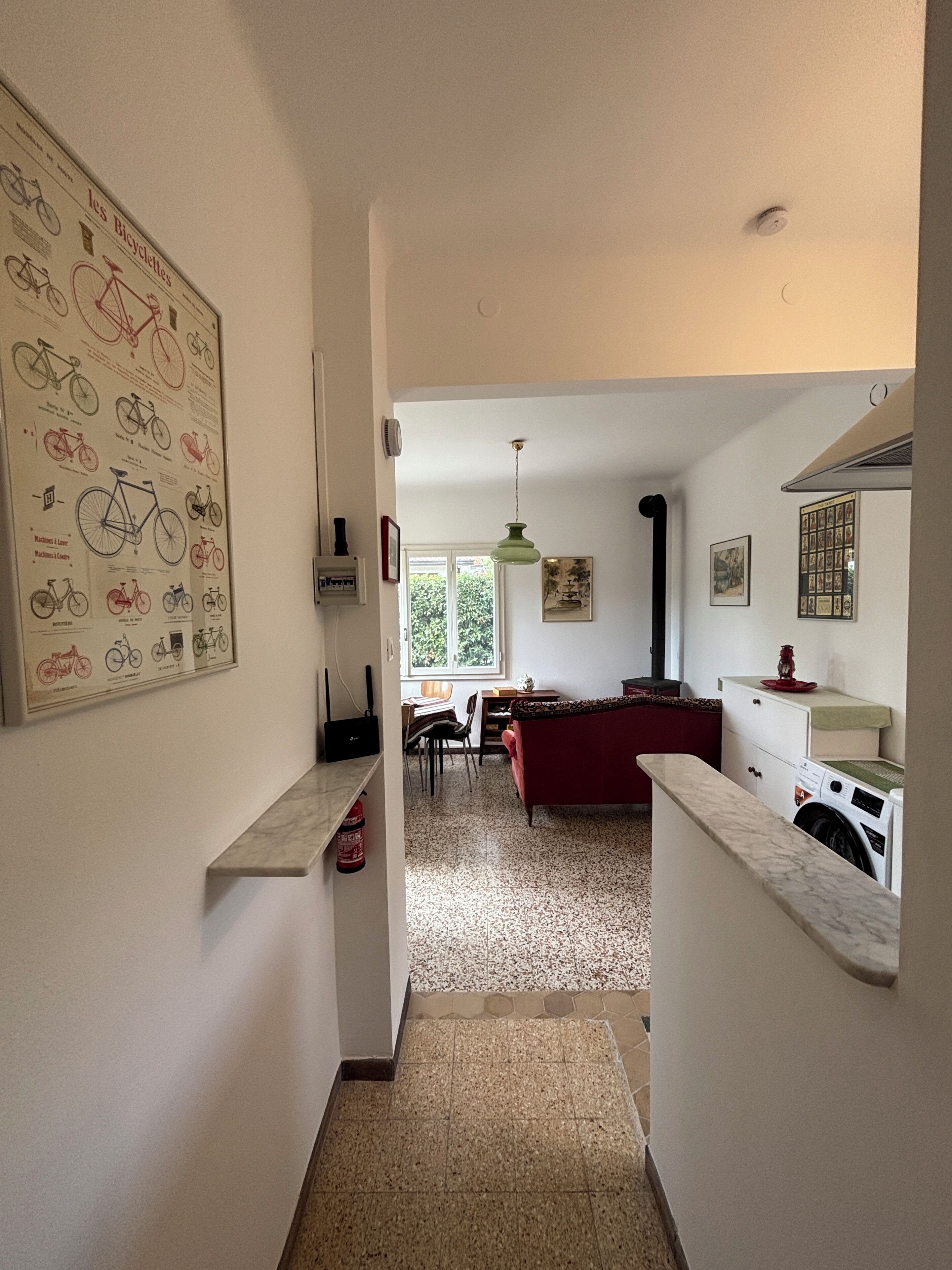 A hallway leading to a living area with a red sofa, a washing machine, and a bicycle-themed wall art.