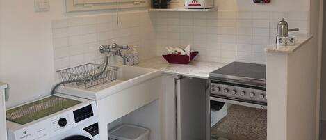 A compact kitchen with a washing machine, a stove, and a window.