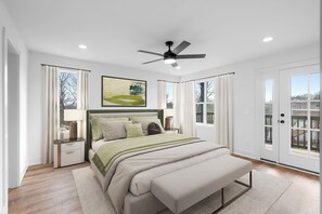 Ein Schlafzimmer mit einem Bett, Nachttischen, einem Deckenventilator und großen Fenstern.