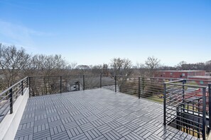 Eine Dachterrasse mit einem Fischgrätmuster-Boden, Metallgeländern und Blick auf ein Backsteingebäude im Hintergrund.