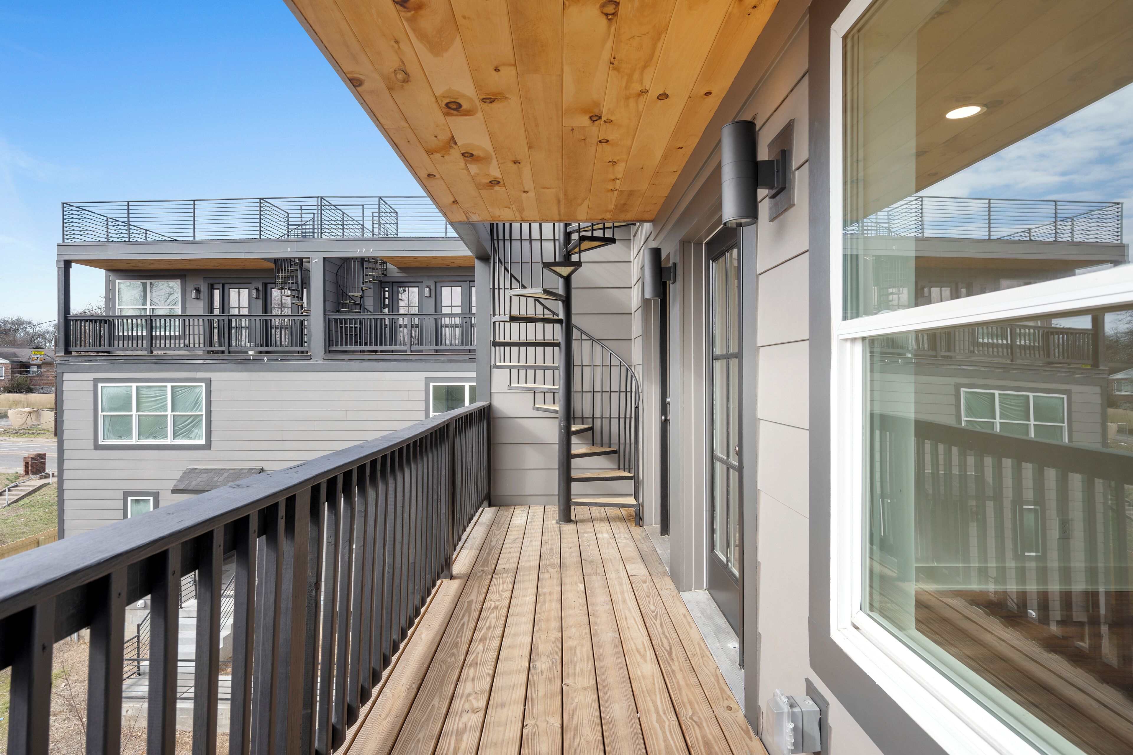 A modern building with a wooden deck, metal railings, and a spiral staircase.