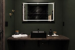 Een badkamer met een donkergroene wand, een rechthoekige spiegel, een zwarte wastafel en een houten aanrecht.