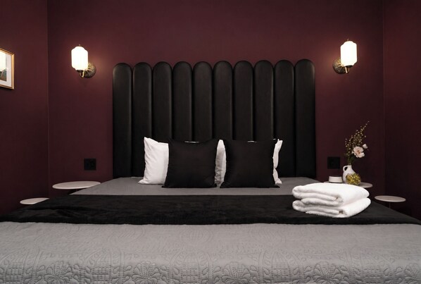 A neatly made bed with a black headboard, white pillows, and a folded white towel on the side.