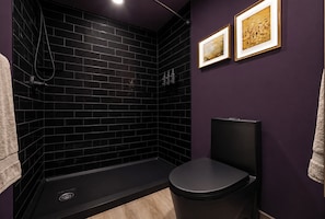 Et moderne badeværelse med en bruseniche med sorte fliser, et toilet og to billeder hængende på væggen.