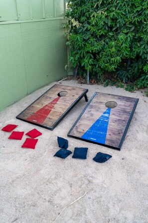 Two wooden bean bags with red and blue sections on a sandy ground, surrounded by greenery. - Family-friendly Farm Retreat near Sequoia & Kings Canyon National Park (Fresno)