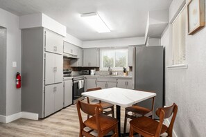 A compact kitchen with grey cabinets, a white countertop, a built-in oven, and a refrigerator. There is a dining table with four chairs. - Family-friendly Farm Retreat near Sequoia & Kings Canyon National Park (Fresno)