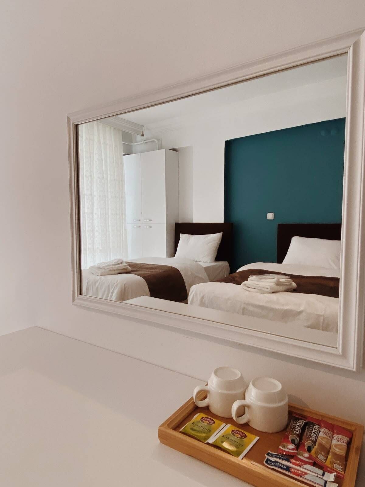 A hotel room with a large mirror reflecting two beds, a wardrobe, and a coffee table with cups and coffee packets.