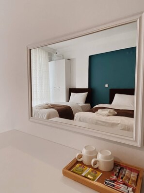 Habitación de hotel con un espejo grande que refleja dos camas, un armario y una mesa de centro con tazas y sobres de café.