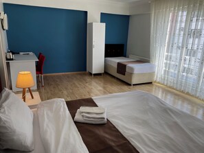 A hotel room with a bed, a desk, a chair, a wardrobe, and a window with curtains.