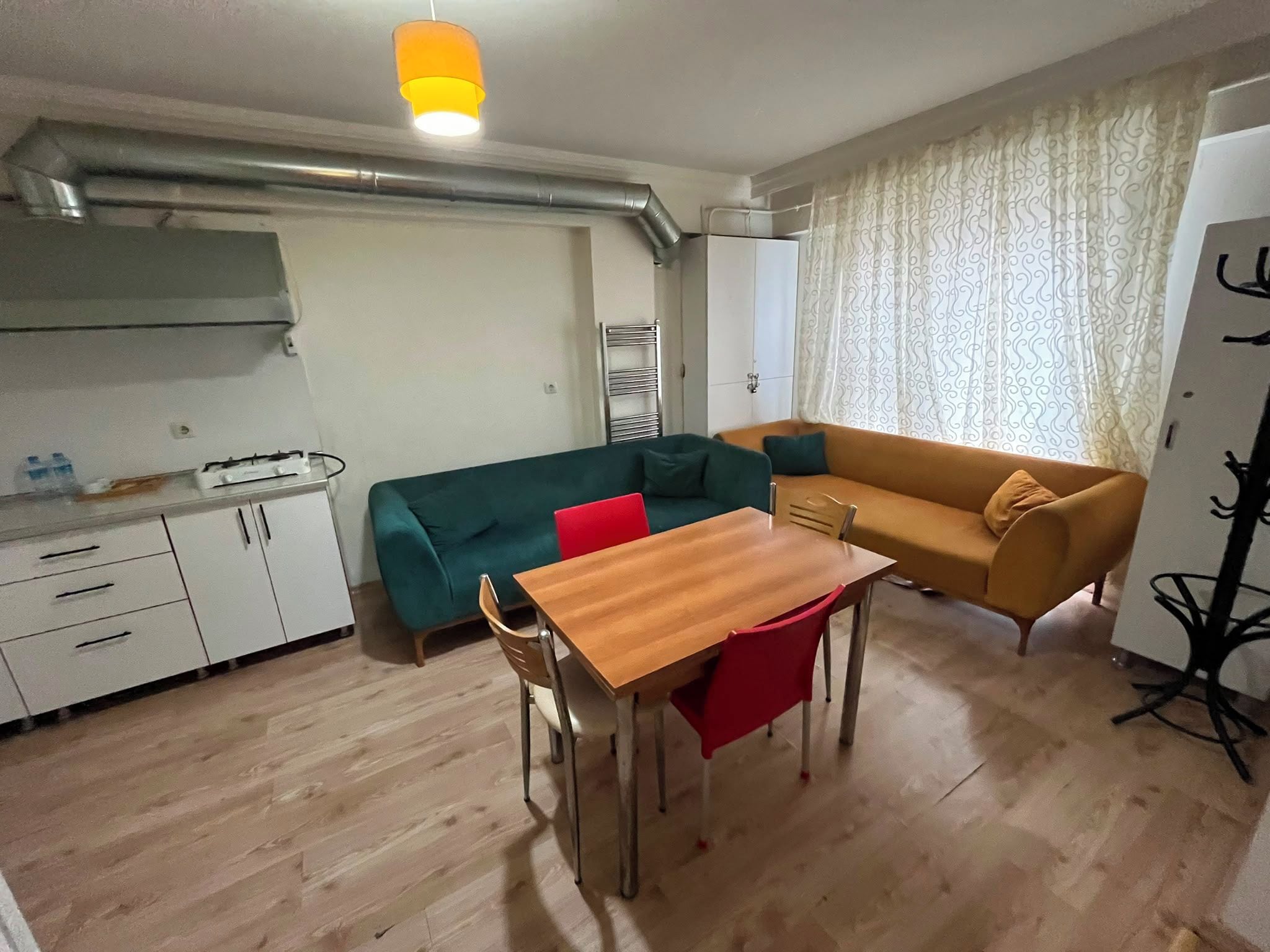 Un espace de vie compact comprenant un coin cuisine, une table à manger avec des chaises, un canapé et un rideau à motifs.