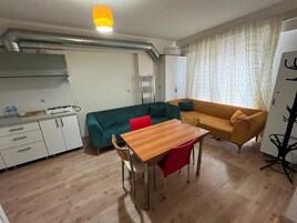 A compact living space with a kitchenette, a dining table with chairs, a sofa, and a patterned curtain.