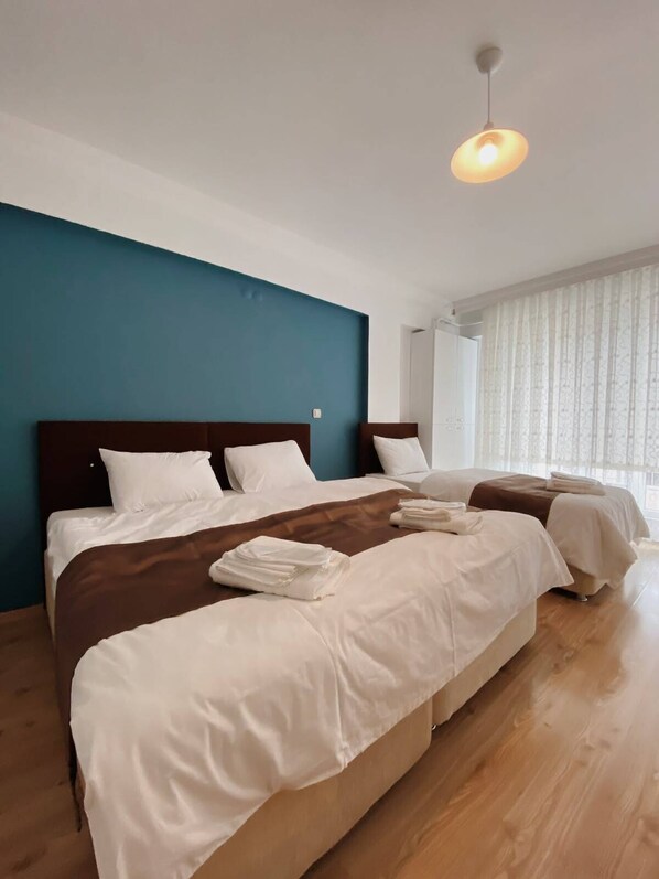 Habitación de hotel con dos camas, una pared de acento azul y un ventanal con cortinas.