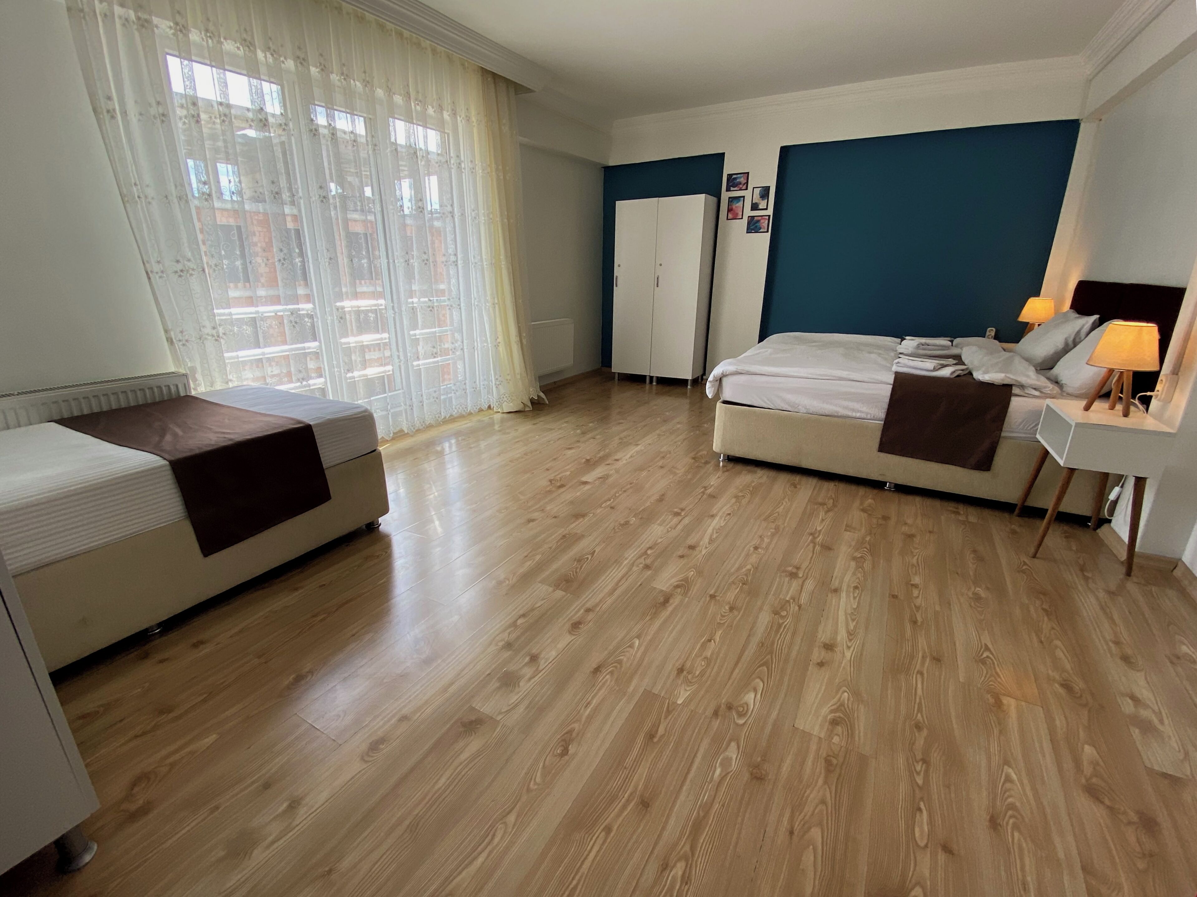 A hotel room with a bed, a bedside table with a lamp, a wardrobe, and a window with curtains.