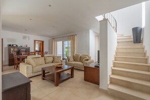 A spacious living area with a sofa set, a coffee table, and a dining table with chairs. A staircase with a black vase is visible in the background. - Holiday Home 'Binitati' with Private Pool, Private Terrace and Private Garden (Sant Lluís)