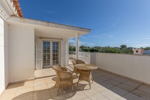 A balcony with a table and chairs, a sliding glass door, and a view of the surrounding area. - Holiday Home 'Binitati' with Private Pool, Private Terrace and Private Garden (Sant Lluís)
