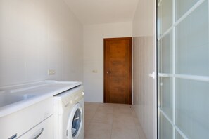 A laundry room with a washing machine and dryer, a wooden door, and a glass shower enclosure. - Holiday Home 'Binitati' with Private Pool, Private Terrace and Private Garden (Sant Lluís)