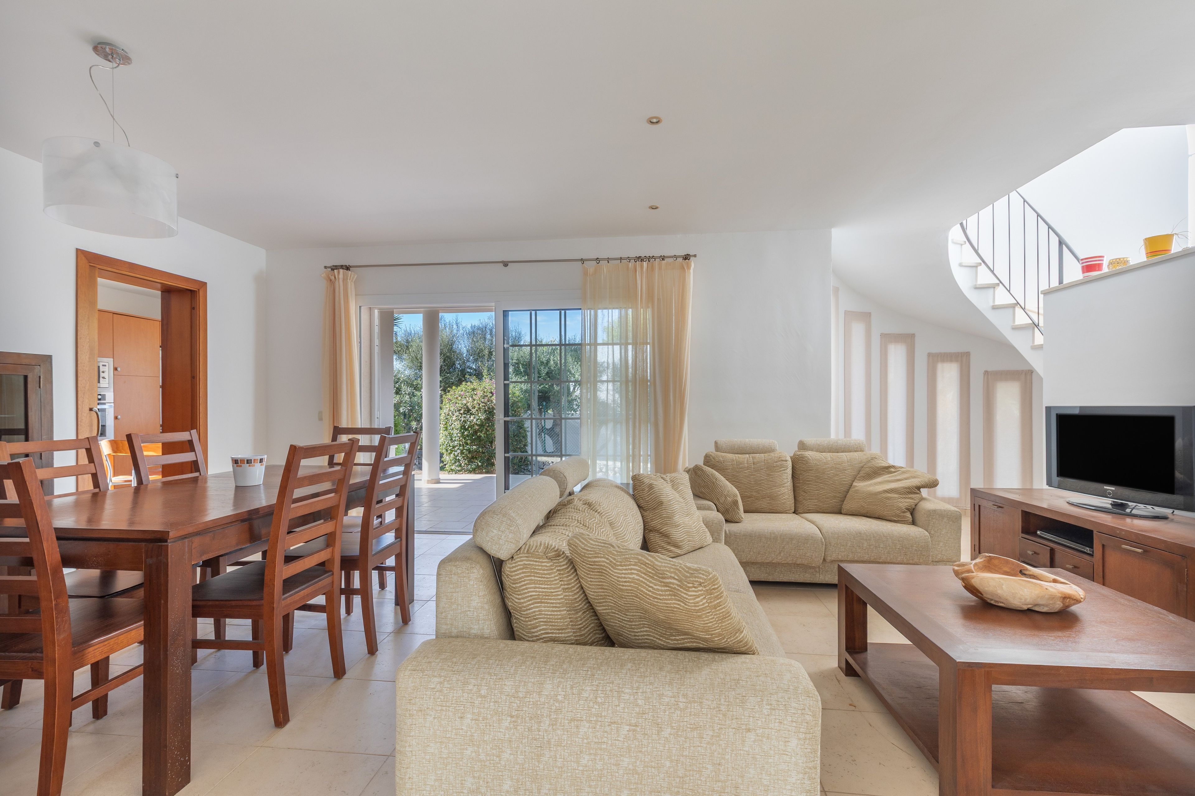 Una sala de estar moderna con un sofá, una mesa de comedor con sillas, un televisor y una escalera.