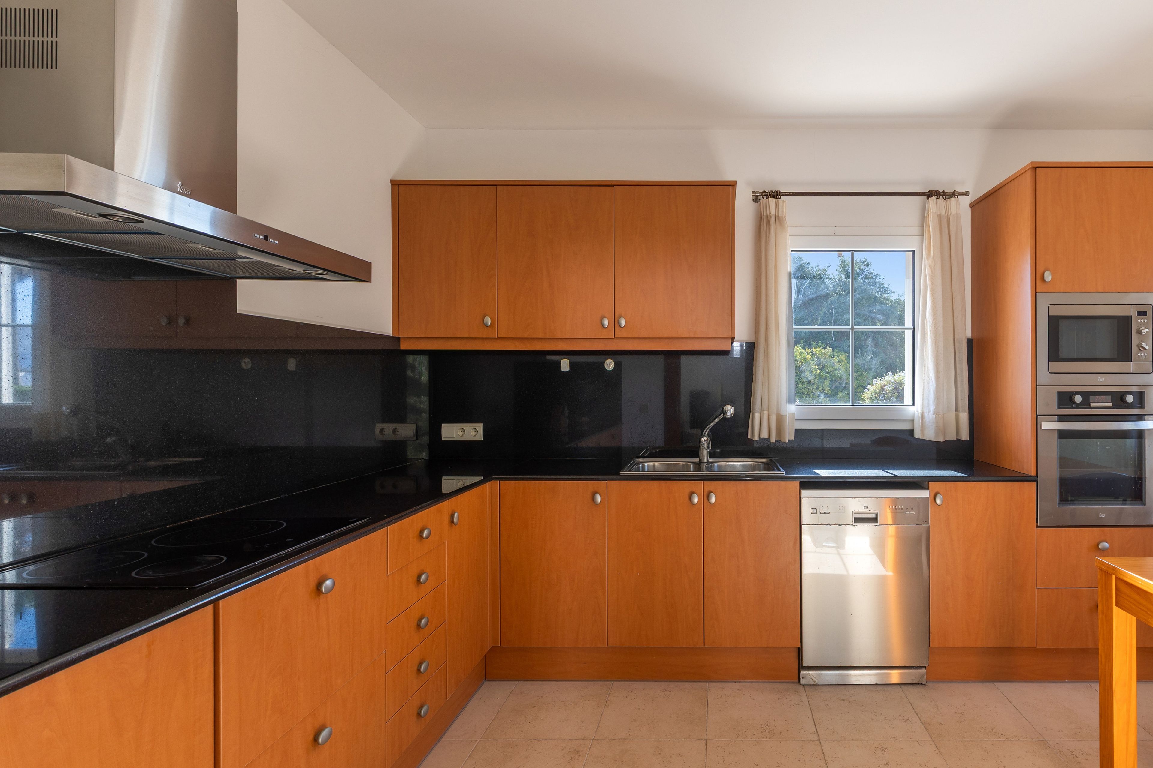 Una cocina moderna con armarios de madera, encimera negra, electrodomésticos de acero inoxidable y una ventana con cortinas.
