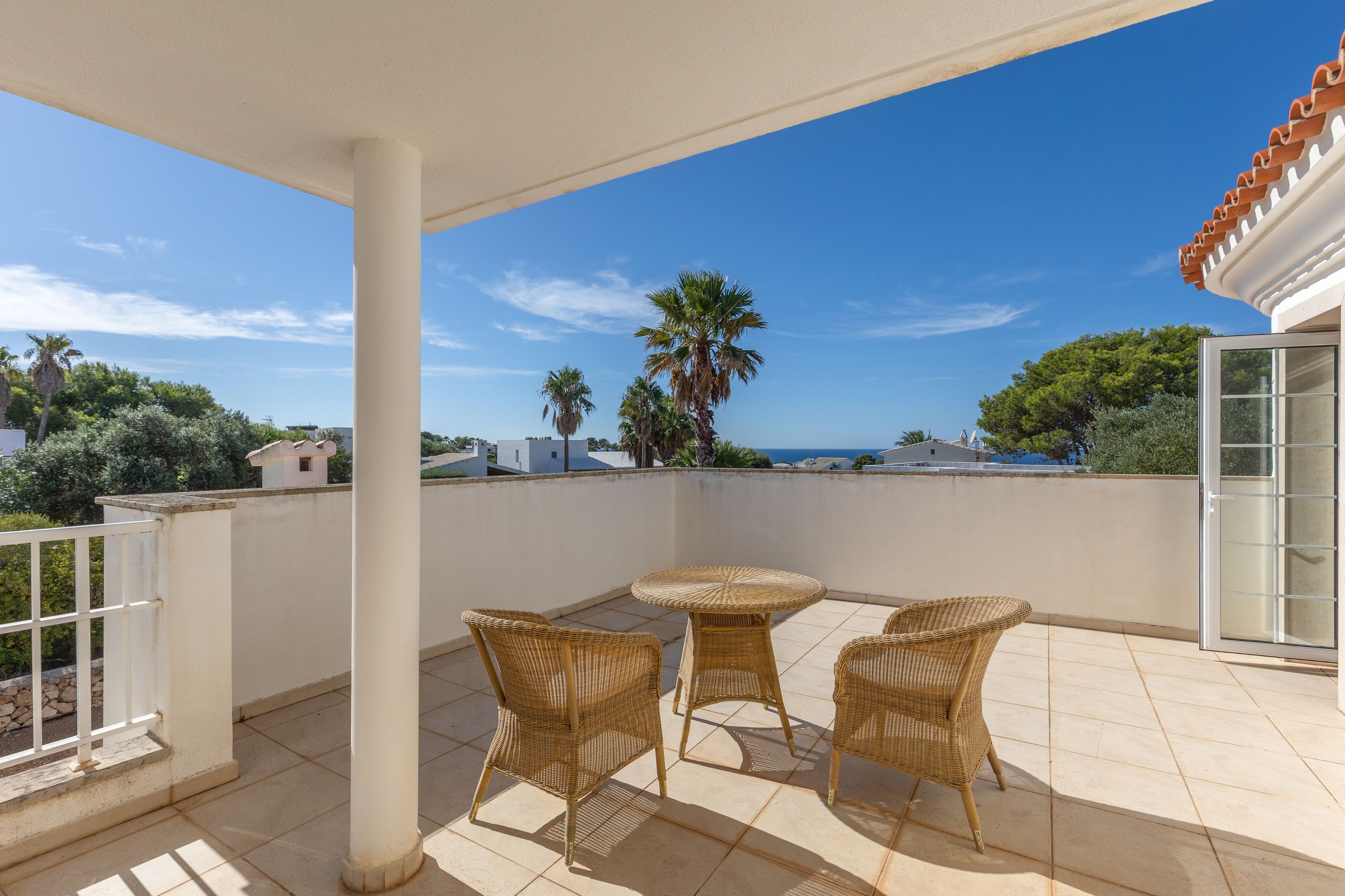 Un espacio de estar al aire libre cubierto, con mobiliario de mimbre y vista al mar.