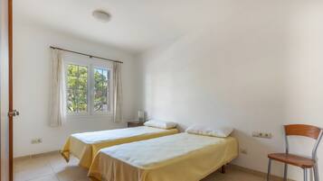 Ein Zimmer mit zwei Einzelbetten, einem Sessel, einem Fenster mit Vorhängen und einem Nachttisch mit einer Lampe.