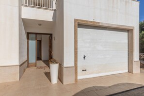A modern building with a large garage door, a balcony, and a potted plant. - Holiday Home 'Binitati' with Private Pool, Private Terrace and Private Garden (Sant Lluís)