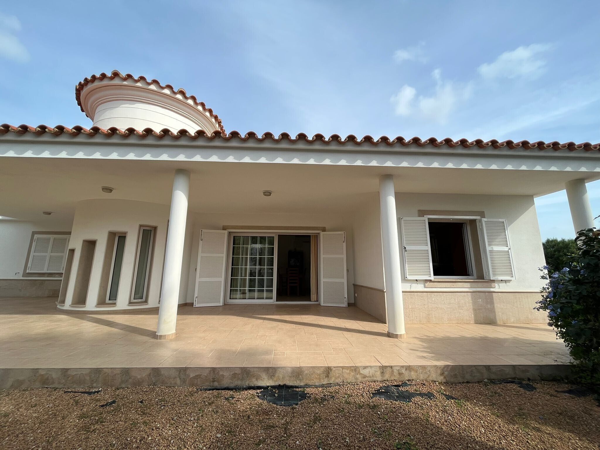 Un espacio al aire libre cubierto, con techo de baldosas, columnas y una puerta que da a un espacio interior.