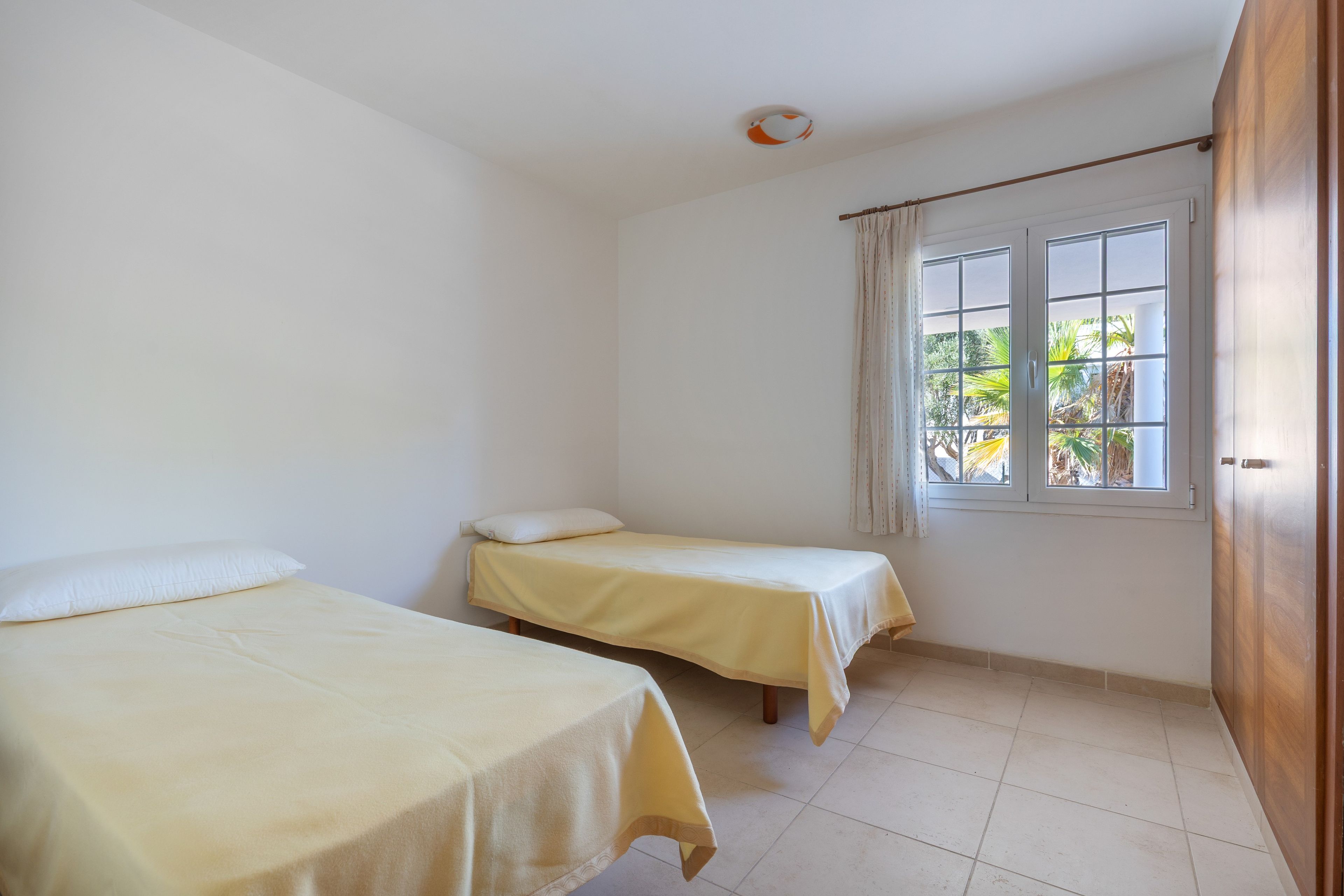 Una habitación con dos camas individuales, una ventana con cortinas y un armario de madera.