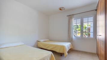 Una habitación con dos camas individuales, una ventana con cortinas y un armario de madera.