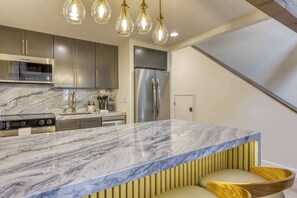 A modern kitchen with a marble countertop, stainless steel appliances, and pendant lighting. - Modern Tahoe Retreat - Your Place to Unwind (South Lake Tahoe)